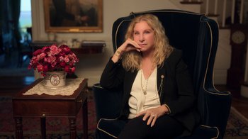 Movie still from “Sidney” (2022), directed by Reginald Hudlin – A woman sitting in a chair in front of a table with flowers; Medium shot, High angle