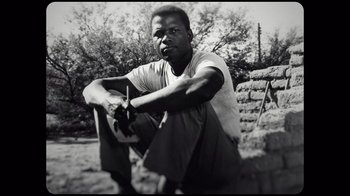 Movie still from “Sidney” (2022), directed by Reginald Hudlin – A black and white photo of a man sitting on the side of a wall; Close Up shot, Low angle