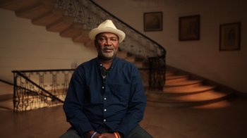 Movie still from “Sidney” (2022), directed by Reginald Hudlin – A man sitting on the ground wearing a hat; Medium shot, Low angle