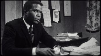 Movie still from “Sidney” (2022), directed by Reginald Hudlin – A black and white photo of a man sitting at a desk; Medium shot, Low angle