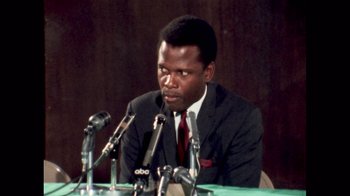 Movie still from “Sidney” (2022), directed by Reginald Hudlin – A man sitting at a table with microphones in front of him; Close Up shot, Low angle