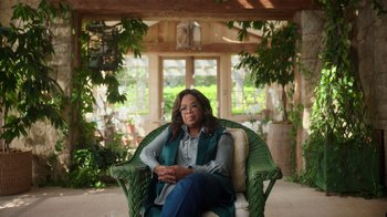 Movie still from “Sidney” (2022), directed by Reginald Hudlin – A woman sitting in a green chair in a room; Wide shot, Low angle