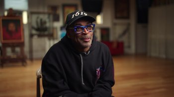 Movie still from “Sidney” (2022), directed by Reginald Hudlin – A man wearing glasses and a hat sitting in a room; Close Up shot, Low angle