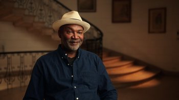 Movie still from “Sidney” (2022), directed by Reginald Hudlin – A man wearing a hat standing next to a staircase; Medium shot, Low angle