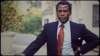 Movie still from “Sidney” (2022), directed by Reginald Hudlin – A man in a suit and tie standing in front of a building; Close Up shot, Low angle