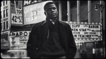 Movie still from “Sidney” (2022), directed by Reginald Hudlin – A black and white photo of a man standing in front of a building; Close Up shot, Low angle