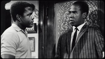 Movie still from “Sidney” (2022), directed by Reginald Hudlin – A black and white photo of two men in a room; Medium shot, Over the shoulder angle