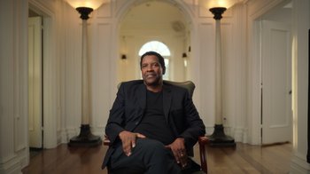 Movie still from “Sidney” (2022), directed by Reginald Hudlin – A man sitting in a chair in front of pillars; Medium shot, Low angle