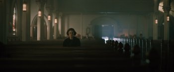 A woman sitting in a church pews in the dark