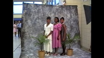 Movie still from “Silver Dollar Road” (2023), directed by Raoul Peck – Three young women posing for a picture in front of a stone wall; Wide shot, High angle