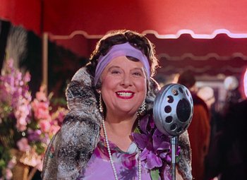 Movie still from “Singin' in the Rain” (1952), directed by Gene Kelly – An older woman in a purple dress holding a microphone in front of her face; Close Up shot, Over the shoulder angle