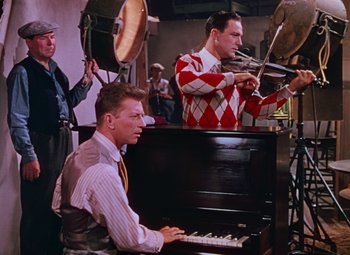 Movie still from “Singin' in the Rain” (1952), directed by Gene Kelly – A man sitting at a piano in front of a group of people; Medium shot, High angle