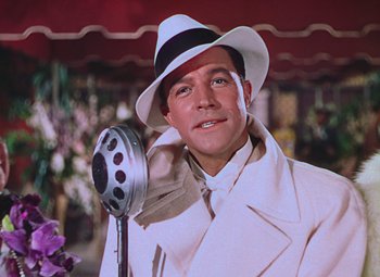 Movie still from “Singin' in the Rain” (1952), directed by Gene Kelly – A man in a white coat and hat holding a microphone; Close Up shot, Low angle