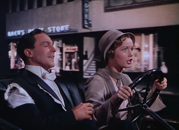 Movie still from “Singin' in the Rain” (1952), directed by Gene Kelly – A man and a woman sitting in a car with a steering wheel; Medium shot, Low angle