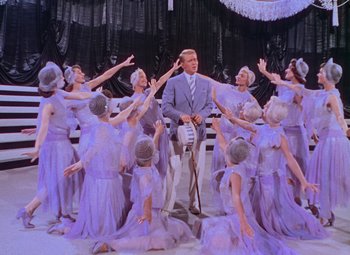 Movie still from “Singin' in the Rain” (1952), directed by Gene Kelly – A group of women in purple dresses and a man in a blue suit; Wide shot, Low angle