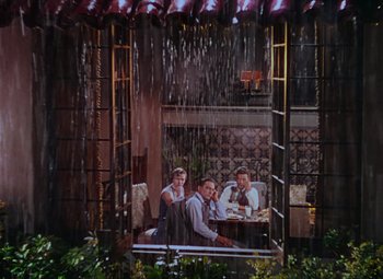Movie still from “Singin' in the Rain” (1952), directed by Gene Kelly – A group of people sitting at a table under a rain shower; Extreme Wide shot, High angle