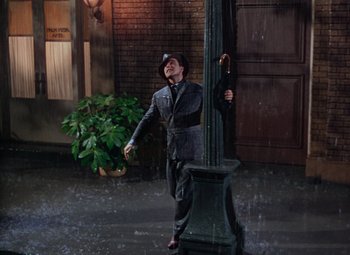 Movie still from “Singin' in the Rain” (1952), directed by Gene Kelly – A man standing next to a street light in the pouring rain; Wide shot, High angle