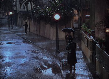 Movie still from “Singin' in the Rain” (1952), directed by Gene Kelly – A person holding an umbrella while standing on the sidewalk; Extreme Wide shot, High angle
