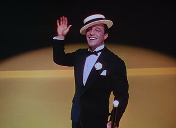 Movie still from “Singin' in the Rain” (1952), directed by Gene Kelly – A man wearing a suit and hat waving; Medium shot, Low angle