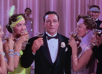 Movie still from “Singin' in the Rain” (1952), directed by Gene Kelly – A man in a tuxedo with two women drinking wine; Medium shot, Low angle