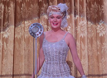 Movie still from “Singin' in the Rain” (1952), directed by Gene Kelly – A woman in a white dress holding a microphone; Medium shot, Low angle