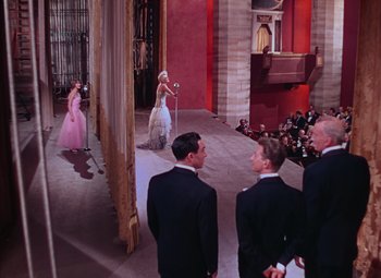 Movie still from “Singin' in the Rain” (1952), directed by Gene Kelly – A group of people standing in front of a woman in a pink dress; Wide shot, High angle