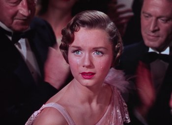 Movie still from “Singin' in the Rain” (1952), directed by Gene Kelly – A young woman in a pink dress crying in front of a group of people; Close Up shot, High angle