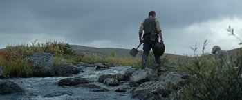 Movie still from “Sisu” (2022), directed by Jalmari Helander – A man standing on top of a rock near a river; Wide shot, Low angle