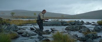 Movie still from “Sisu” (2022), directed by Jalmari Helander – A man standing on a rock in the water holding a plate; Medium shot, Low angle