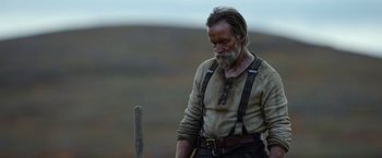 Movie still from “Sisu” (2022), directed by Jalmari Helander – An old man with long hair and a beard is looking down at a pole; Medium shot, Low angle