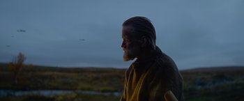 Movie still from “Sisu” (2022), directed by Jalmari Helander – A man with long hair and a long beard is standing in a field; Close Up shot, Low angle