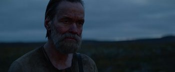 Movie still from “Sisu” (2022), directed by Jalmari Helander – An old man with a beard is standing in the dark; Close Up shot, Over the shoulder angle
