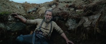 Movie still from “Sisu” (2022), directed by Jalmari Helander – An older man with a long beard laying on the ground; Medium shot, Low angle