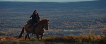 Movie still from “Sisu” (2022), directed by Jalmari Helander – A man riding a horse on top of a hill; Wide shot, Low angle