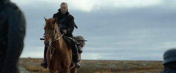 Movie still from “Sisu” (2022), directed by Jalmari Helander – A man riding on the back of a brown horse; Medium shot, Low angle