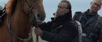 Movie still from “Sisu” (2022), directed by Jalmari Helander – A man with a beard is petting a horse's nose; Close Up shot, Low angle