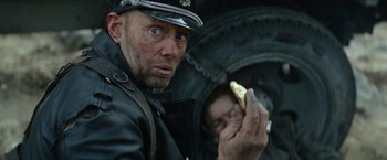Movie still from “Sisu” (2022), directed by Jalmari Helander – A man in a german military uniform holding a banana; Close Up shot, Over the shoulder angle