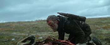 Movie still from “Sisu” (2022), directed by Jalmari Helander – A man with a knife in his mouth and a bunch of blood on his face; Medium shot, Over the shoulder angle
