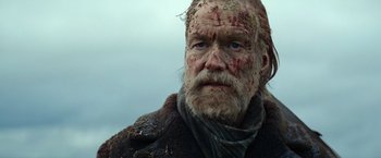 Movie still from “Sisu” (2022), directed by Jalmari Helander – A person with a beard and face covered in blood; Close Up shot, Low angle