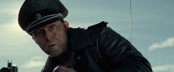 Movie still from “Sisu” (2022), directed by Jalmari Helander – A person wearing a hat and a leather jacket; Close Up shot, Low angle