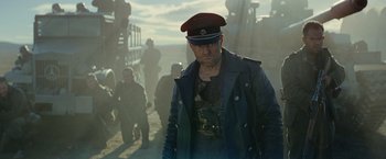 Movie still from “Sisu” (2022), directed by Jalmari Helander – A man in a military uniform is standing in front of a group of people; Medium shot, Low angle