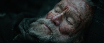 Movie still from “Sisu” (2022), directed by Jalmari Helander – An old man with a beard is laying on the ground; Close Up shot, Overhead angle