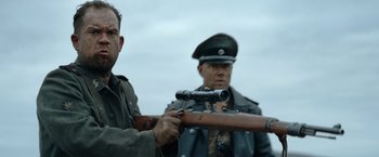 Movie still from “Sisu” (2022), directed by Jalmari Helander – Two men in military garb are holding a rifle; Close Up shot, Over the shoulder angle