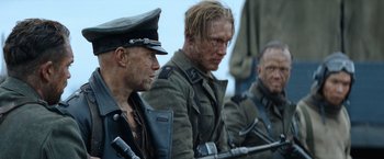Movie still from “Sisu” (2022), directed by Jalmari Helander – A group of men sitting next to each other on top of a field; Medium shot, Low angle