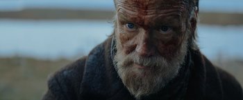 Movie still from “Sisu” (2022), directed by Jalmari Helander – An old man with a beard and blue eyes looking at the camera; Close Up shot, Low angle