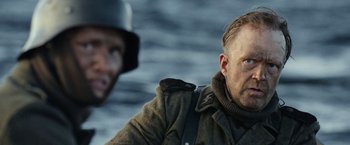 Movie still from “Sisu” (2022), directed by Jalmari Helander – A person wearing a hat and a jacket; Close Up shot, Over the shoulder angle