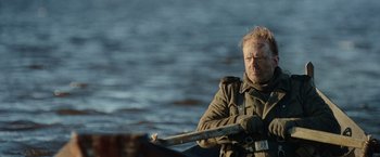 Movie still from “Sisu” (2022), directed by Jalmari Helander – A man holding a wooden stick while standing in a boat; Close Up shot, Over the shoulder angle