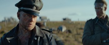 Movie still from “Sisu” (2022), directed by Jalmari Helander – A man in a leather jacket wearing a hat; Close Up shot, Low angle
