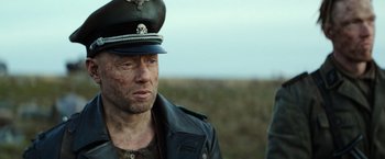 Movie still from “Sisu” (2022), directed by Jalmari Helander – A man wearing a military uniform and a hat; Close Up shot, Over the shoulder angle