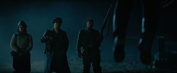Movie still from “Sisu” (2022), directed by Jalmari Helander – Two men standing next to each other holding a gun; Medium shot, Low angle